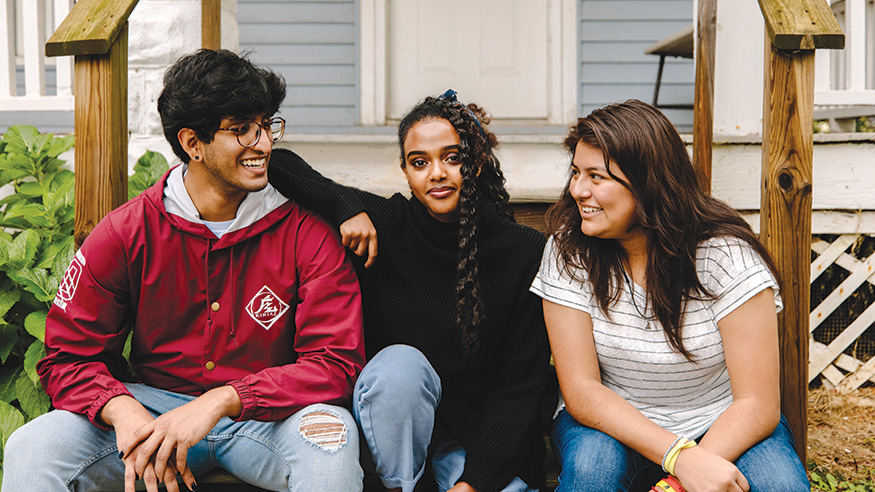 Three students sitting in front of a house