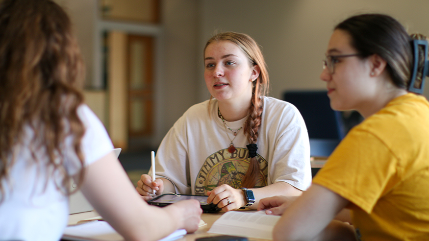 Three female students talk around a table with textbooks