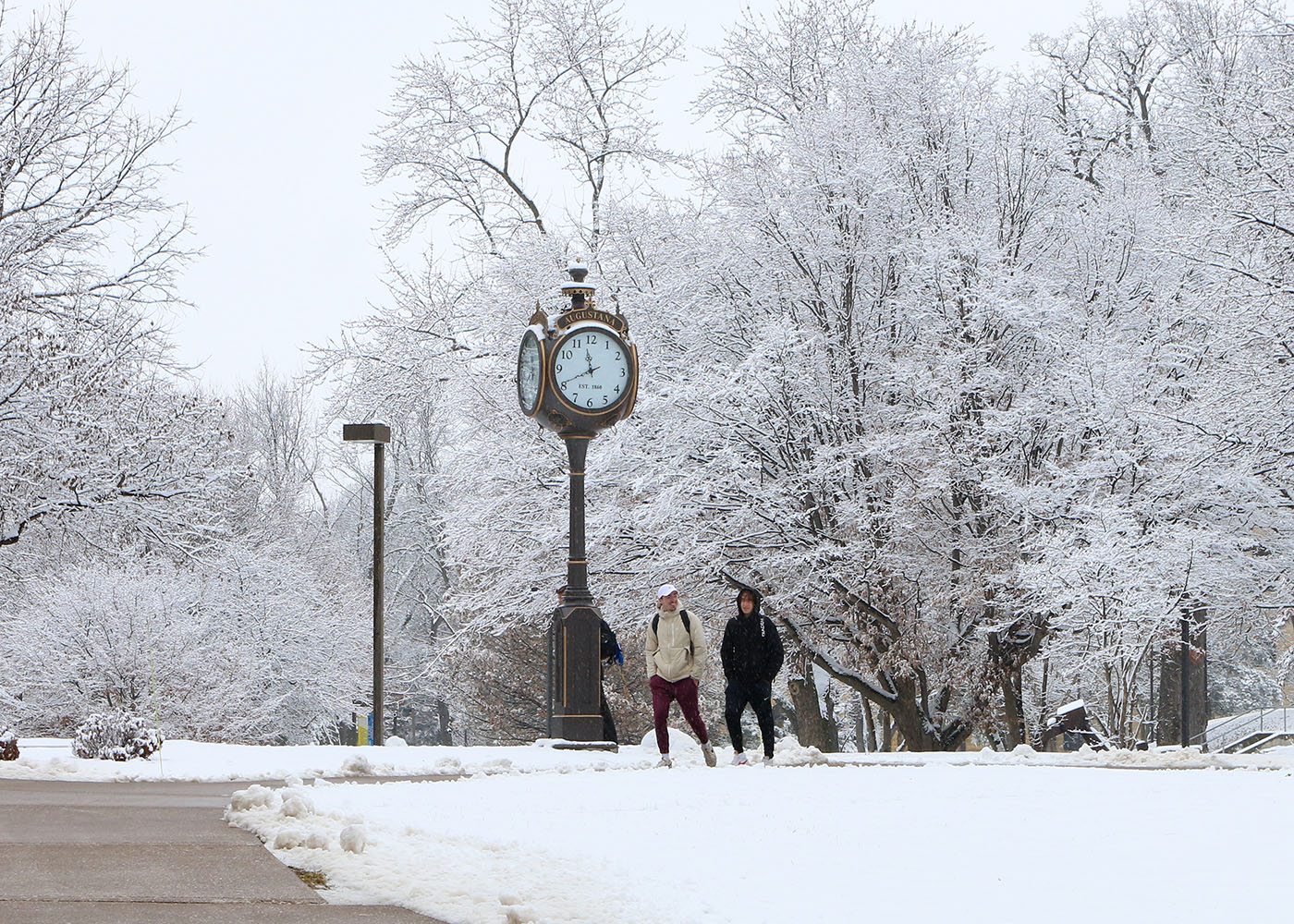 two students walking by a clock on a snowy campus