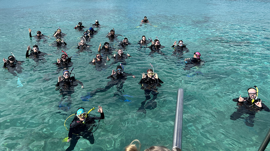 A class of students wave at the camera while in the waters of Bonaire