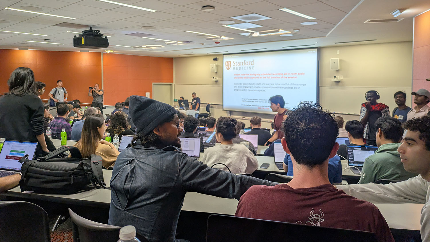 a wide shot of a classroom at Stanford. Shows students and a projection Screen