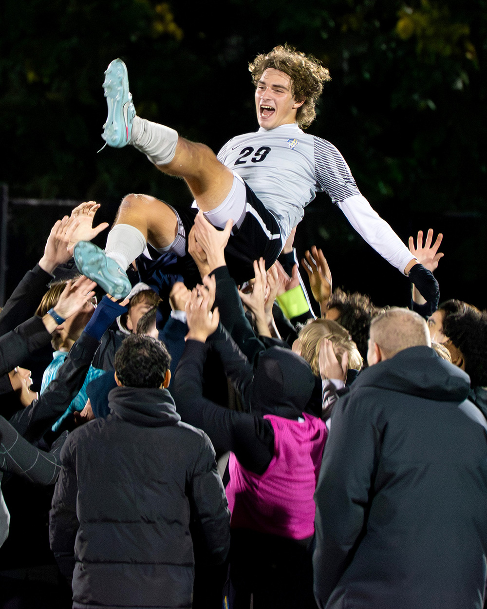 A soccer player is hoisted into the air by a crowd of people after a game