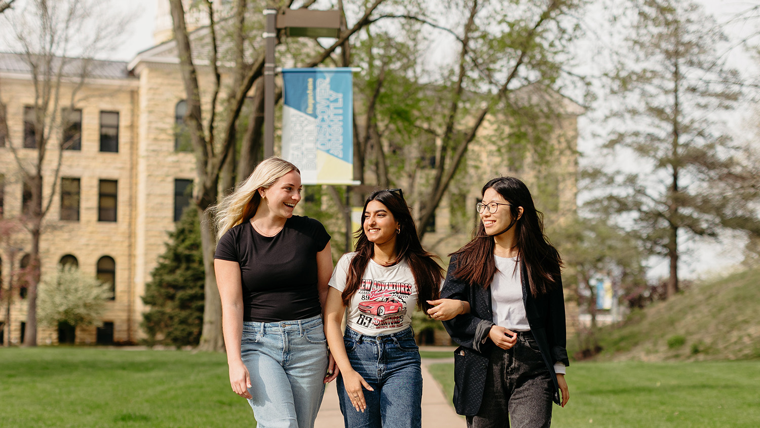 Three students walking through the Quad, arm-in-arm