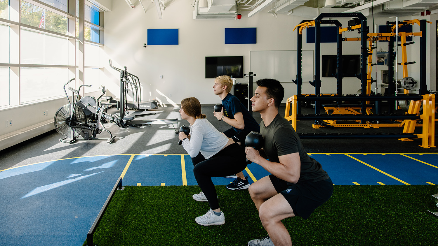 Three students do dumbbell squats in the fitness room