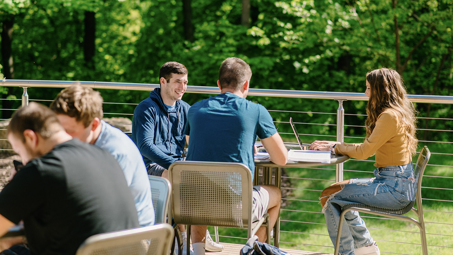 Three students talk at a table on the coffee shop balcony