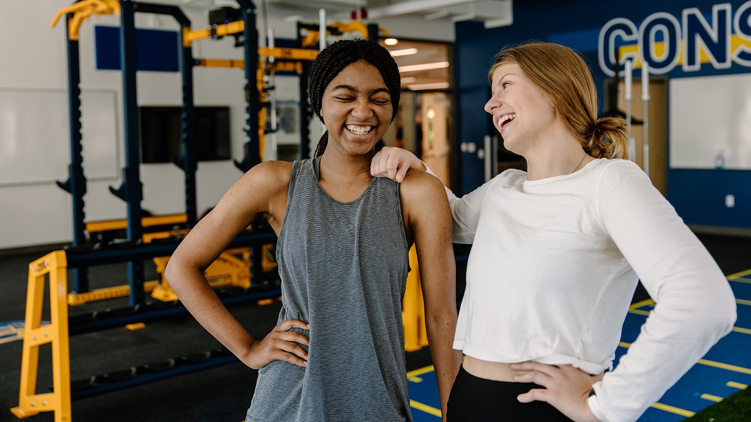 Two students laugh in the weight room