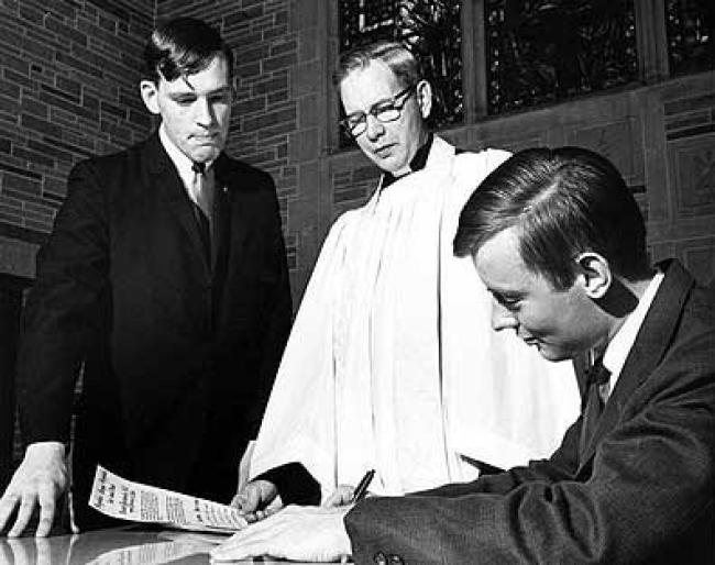 Signing the Campus Church charter in 1966. Pictured are the Rev. Arnold Carlson, who advised students until they called a pastor; standing at left, Kent Anderson; seated at right, Allan Rohlfs.