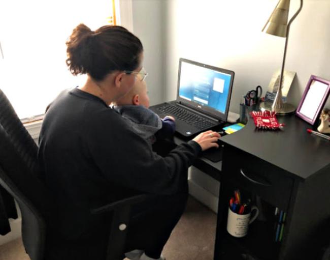 Bri sitting with her son on her lap typing on the laptop in front of her