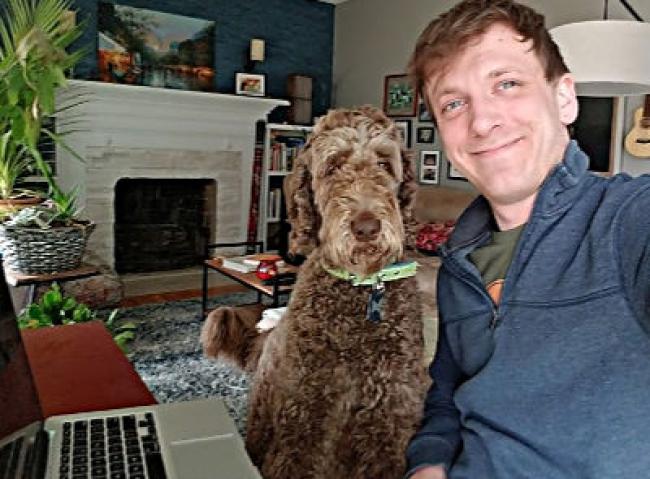 Laptop keys, golden doodle and Kevin smiling with plants and fireplace in background.