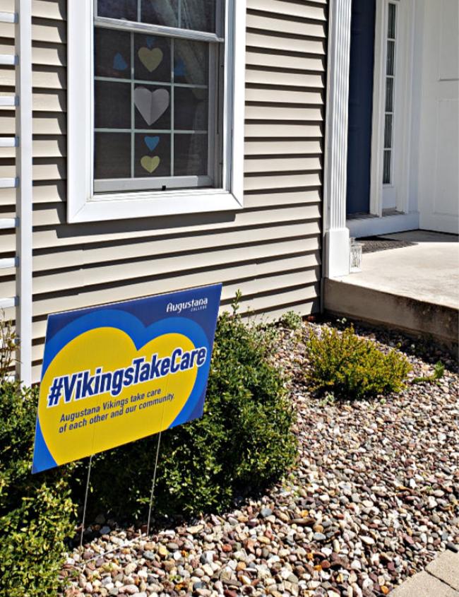 Blue and yellow Augustana sign to the left. Window in the background with hearts taped to the window