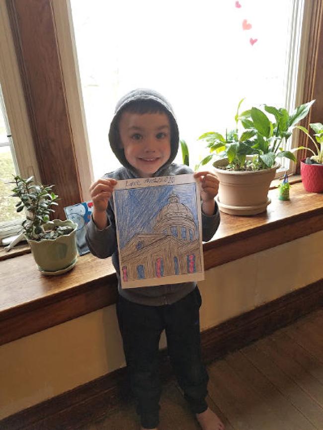 boy standing in front of the window showing off the picture he colored