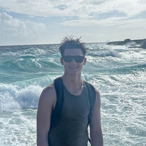 A man posing for a photo with the ocean and waves in the background